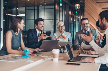 Group of people at work talking around a table with their laptops open